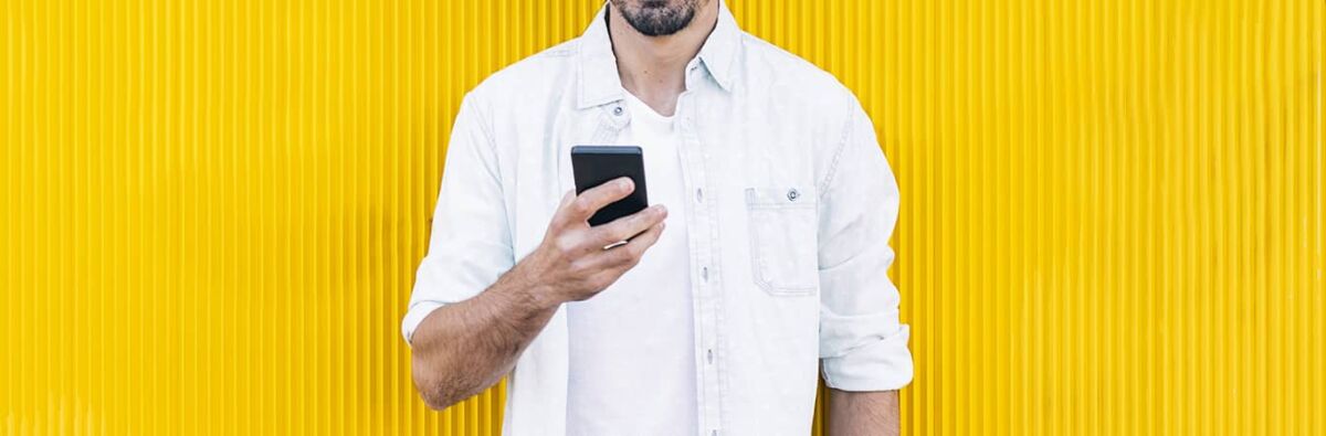 Man with beard standing by yellow wall with phone in his hands