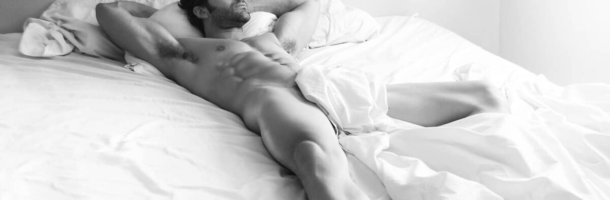 Muscular man with abs and beard lying in bed naked