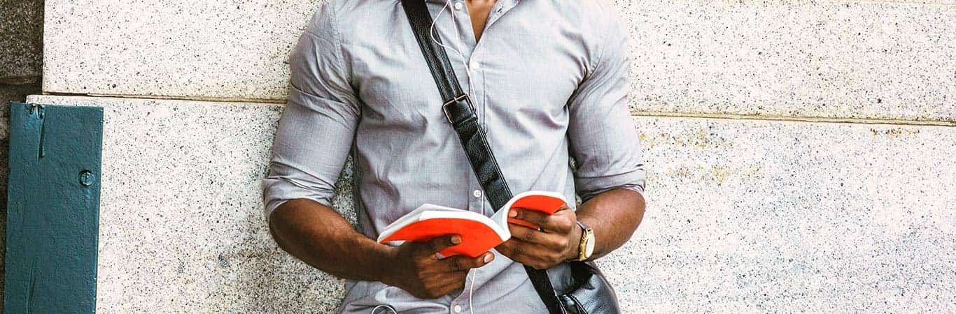 gay man leaning against wall reading a red book