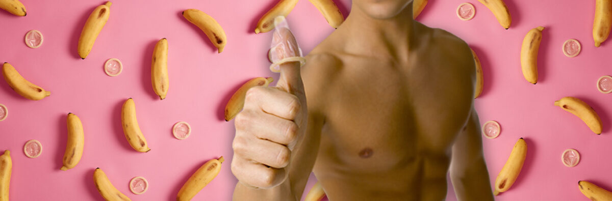 Shirtless man with condom on thumb, on pink background with bananas and condoms