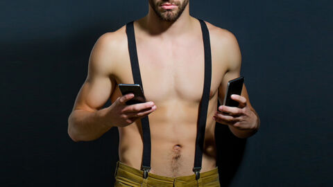 Shirtless man holding two phones