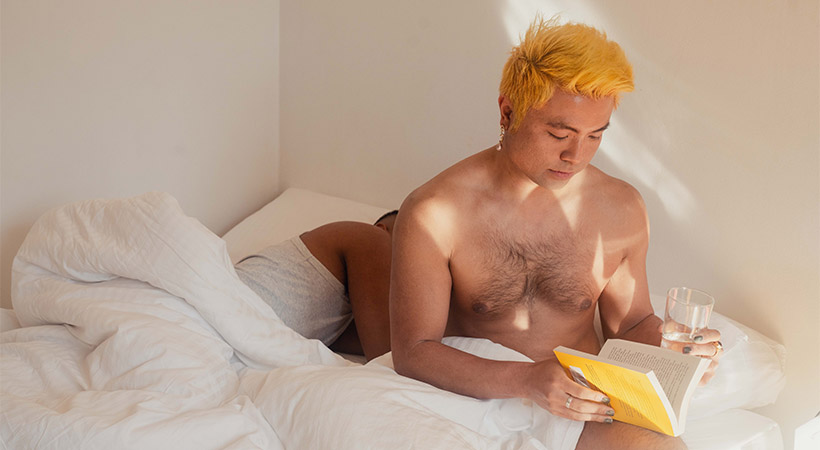 vietnamese-cambodian-man-reads-book-in-bed-with-partner-sleeping