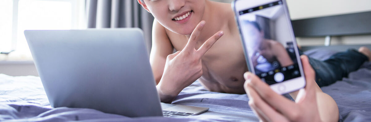 young shirtless man on bed with laptop taking selfie