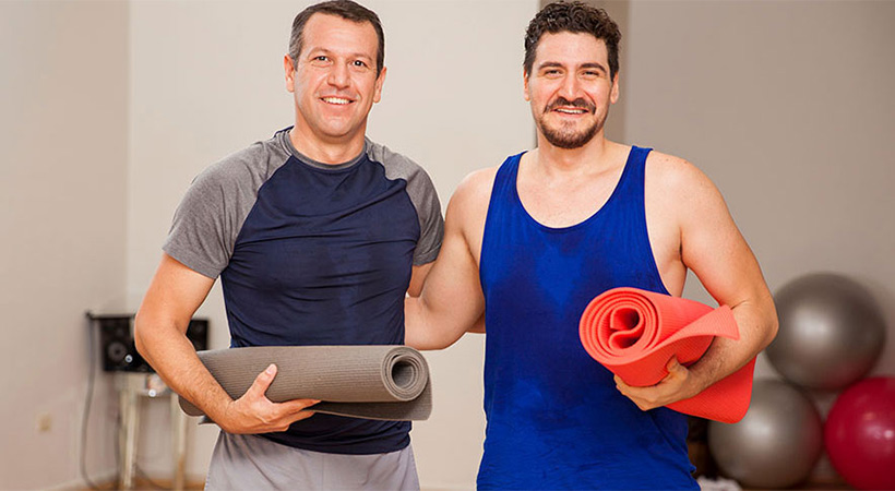 two men carrying yoga matts after a workout