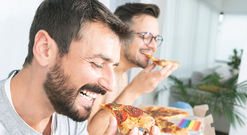 two male friends share a pizza together at home