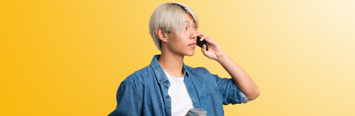Man with bleached hair has important conversation on mobile phone holding coffee cup