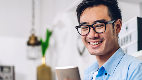 happy man with glasses looks at his mobile phone at home