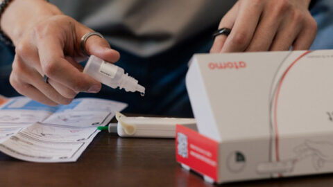 Mans hands holding liquid dropper for HIV self test, box and instructions on table