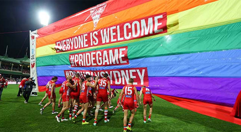Australian afl players on field at pride game holding up giant rainbow flag