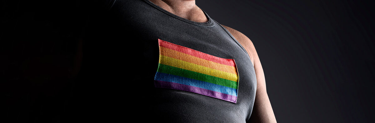 sports athlete in partial darkness wearing charcoal singlet with rainbow pride flag on chest