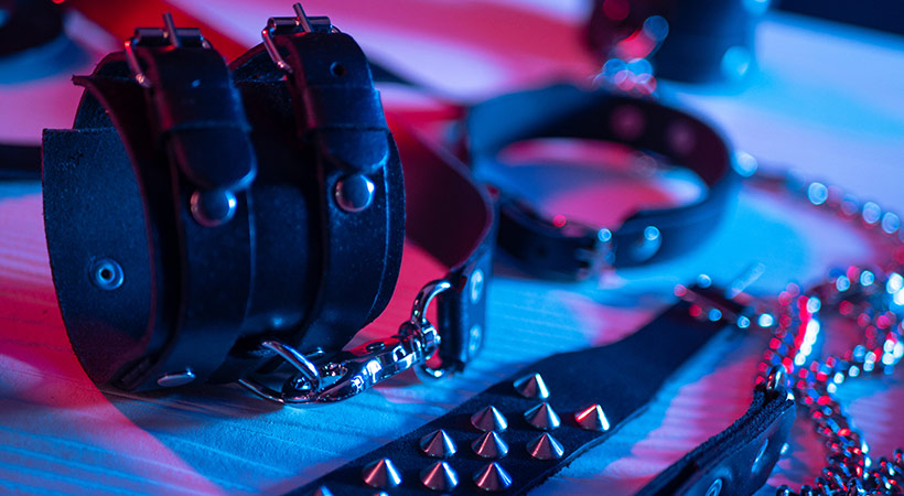 bdsm leather handcuffs and restraints with chains bathed in pink and blue neon lighting