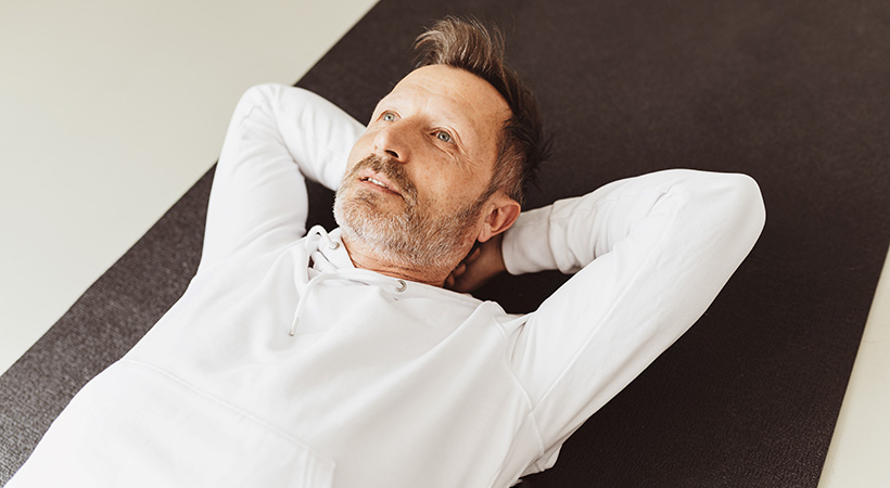 man lies down on floor focussing on pelvic floor exercises