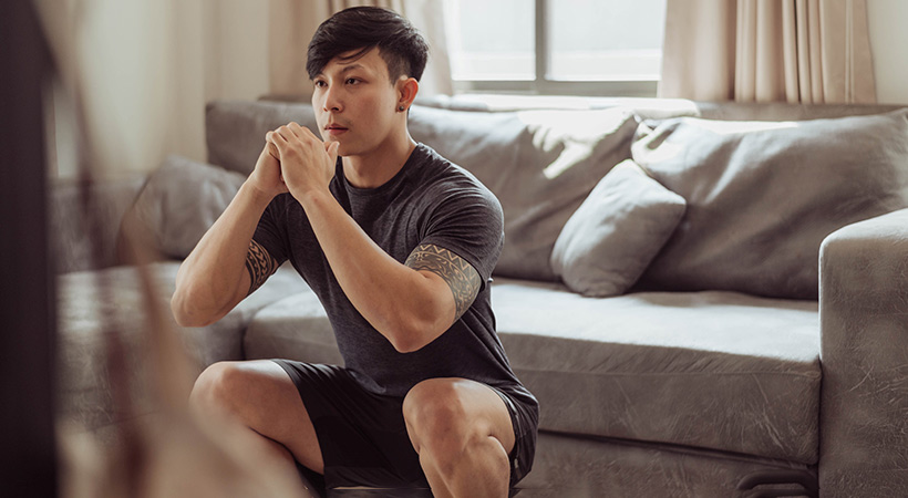 man with arm tattoos exercises in living room doing squats