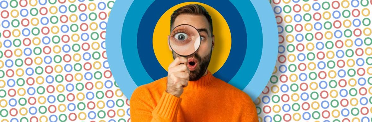 Man in orange sweater holds magnifying glass in front of emen8 logo