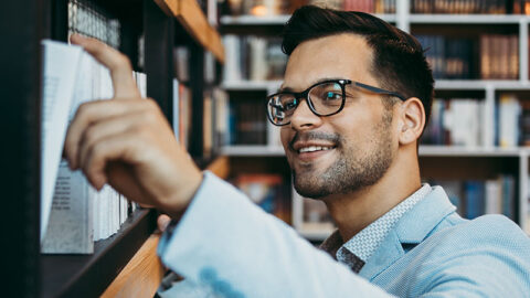 Suited man with glasses takes book from library shelf