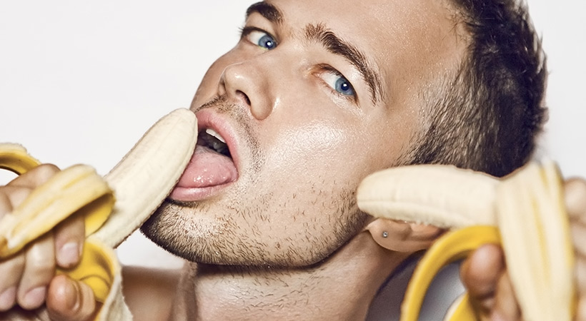 blue eyed man seductively licks two bananas