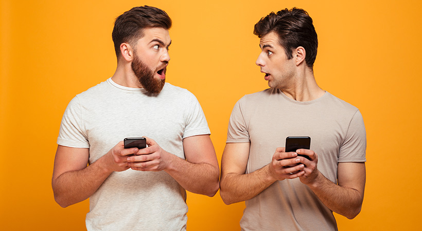 two guys on mobile phones look at each other in surprise