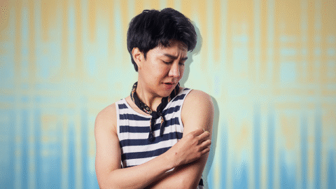 thai-man-scratching-mpox-sore-arm-blue-yellow-background