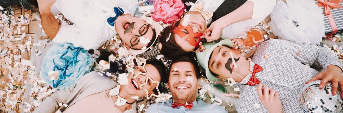 five gay friends lay on floor laughing among pride party confetti