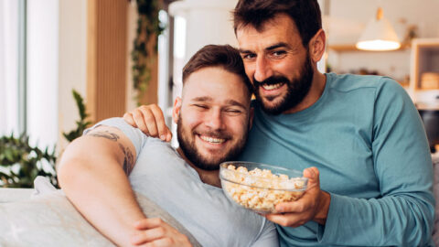 gay couple snuggle up together with popcorn and a movie