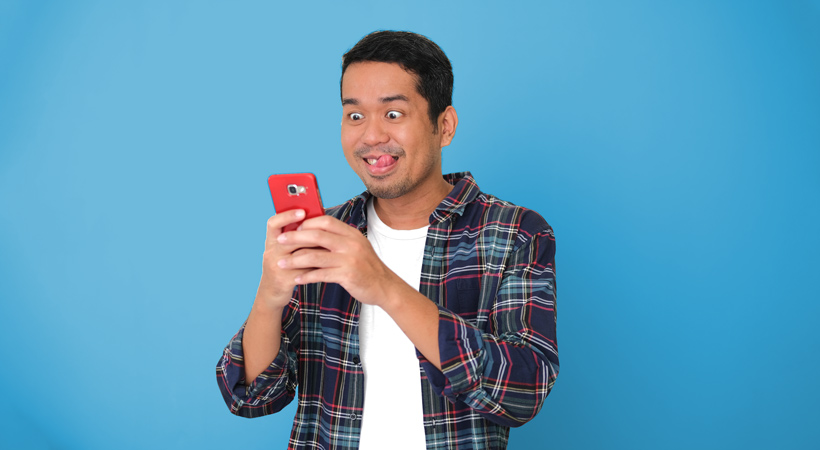asian man looks eagerly at his mobile phone with his tongue sticking out