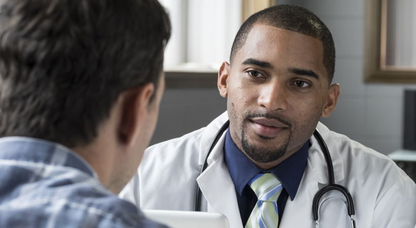 man sits opposite friendly doctor during health check