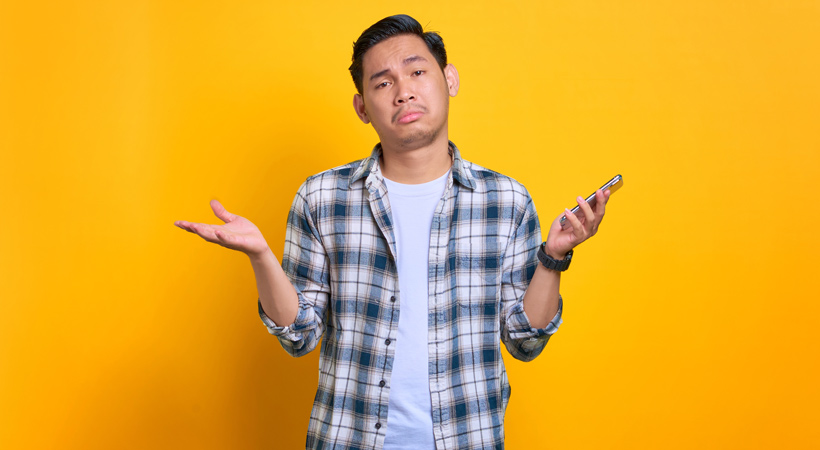 young asian man holds mobile phone and shrugs