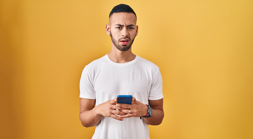 young man holds mobile phone looking confused