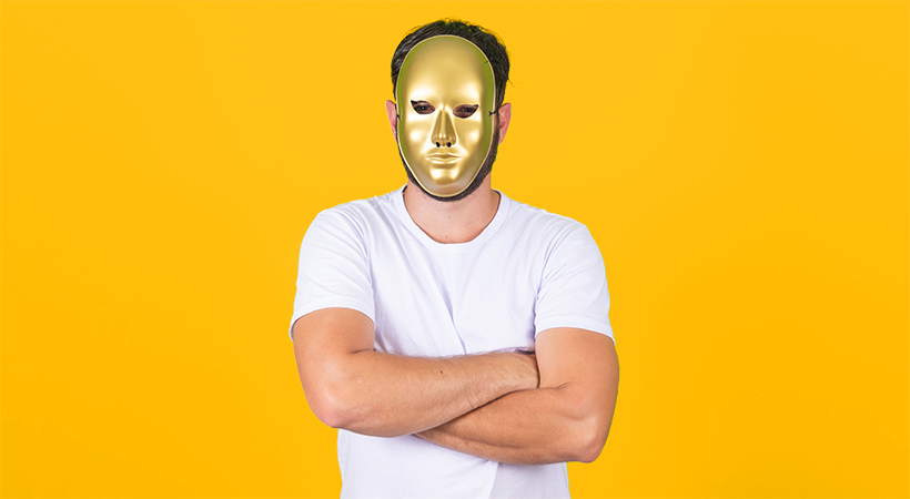 man with arms folded wears gold mask