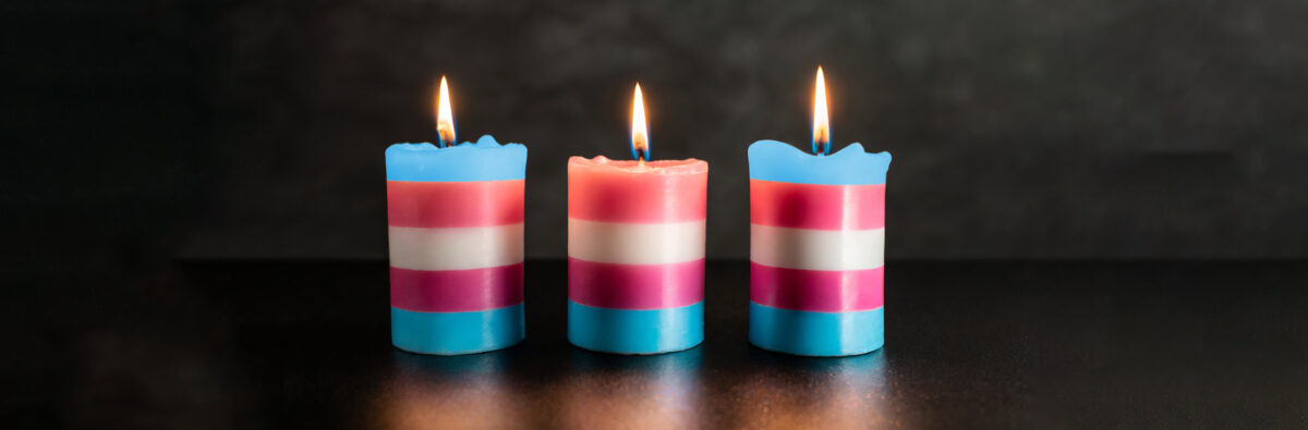 Three lit candles in the trans flag colours for transgender day of remembrance