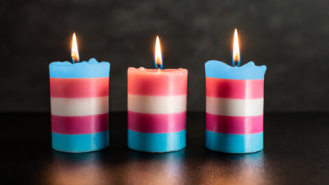 Three lit candles in the trans flag colours for transgender day of remembrance
