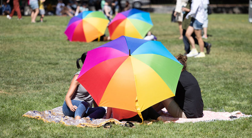 people under rainbow umbrella at springout pride community picnic canberra