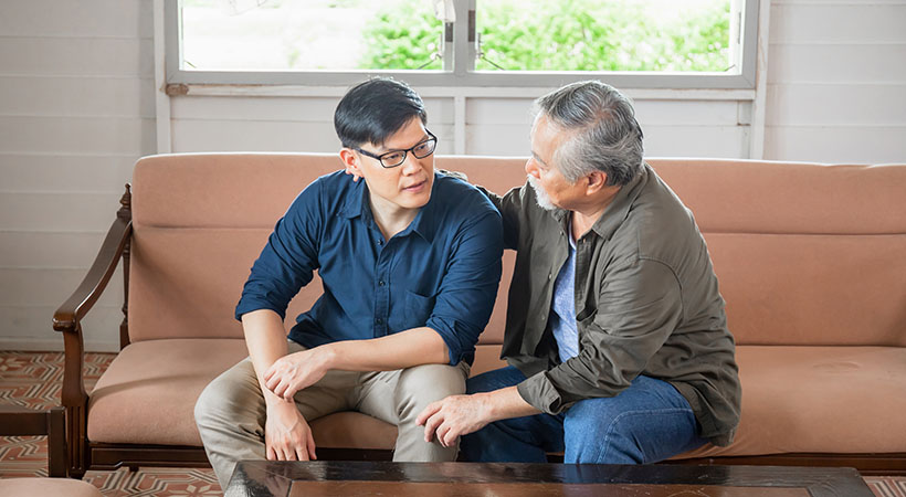 Senior Asian father gives advice to adult son in living room