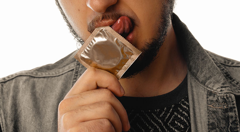 Sexy unshaved gay man with condom in his mouth isolated on white background