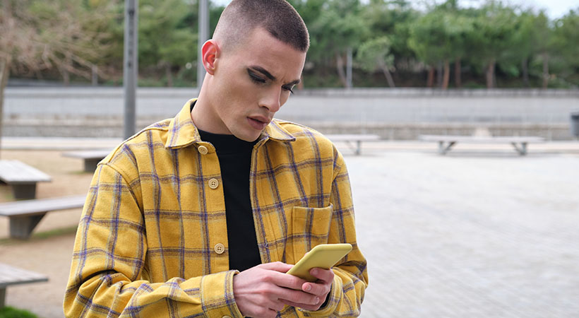 young white man wearing make up, chatting on his smartphone annoyed.