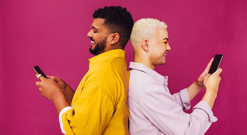 interracial-couple-on-phones-with-backs-together-on-pink-background