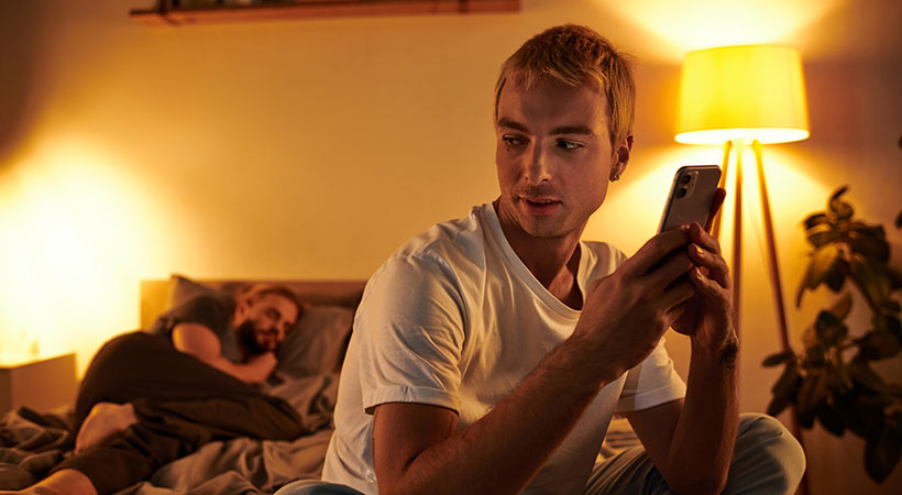 man-secretively-messaging-while-partner-sleeps-in-bed