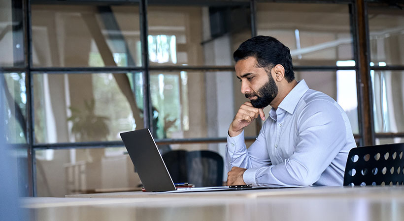 south-asian-man-thoughtfully-researching-on-laptop