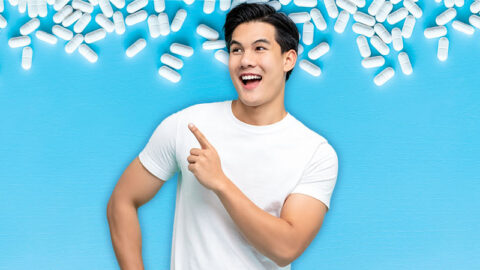 young-asian-man-in-white-t-shirt-points-excitedly-pills-on-blue-background