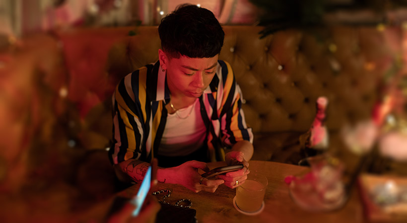 A non-binary person using their cellphone at a bar