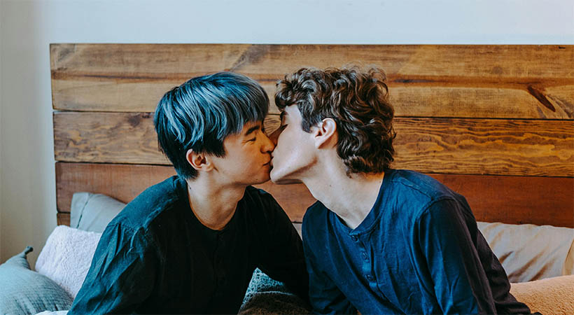 Asian man and white non-binary person kiss in bed