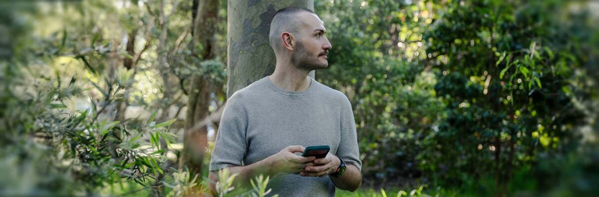 White man on his phone in a park looking in the distance