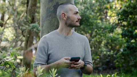 White man on his phone in a park looking in the distance