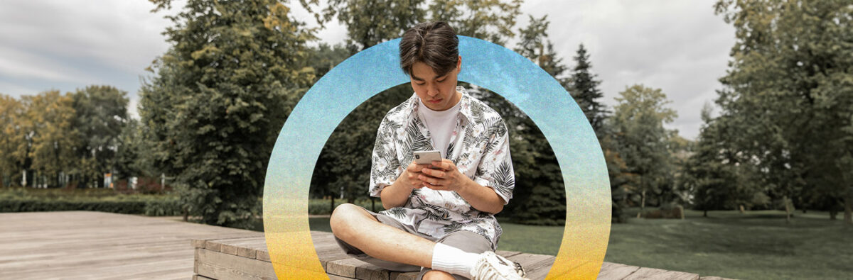 Young Asian man sitting in park on phone