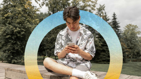 Young Asian man sitting in park on phone