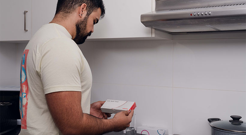 Venezuelan man holding HIV self test kit in kitchen 