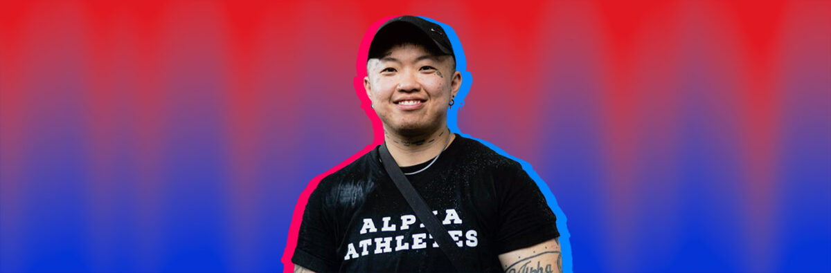 Happy Chinese trans man in black t-shirt smiling, on red and blue textured background