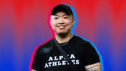 Happy Chinese trans man in black t-shirt smiling, on red and blue textured background