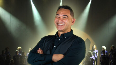 Maori comedian smiling with stage performance in background