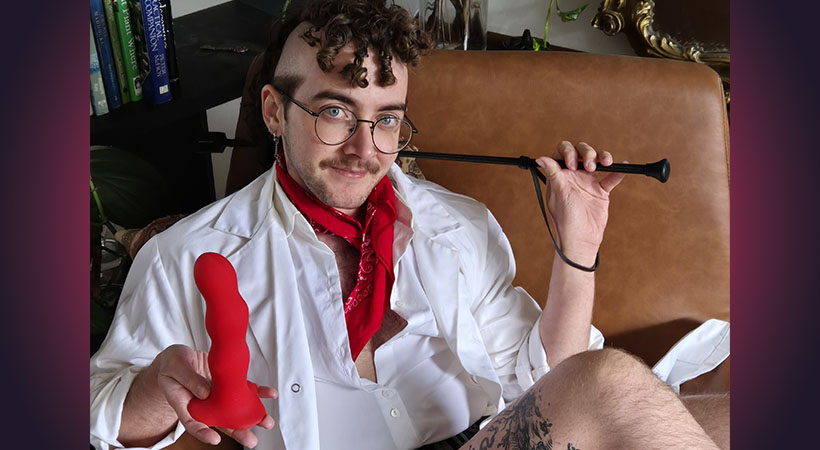White transmasc person in white coat holding a red dildo